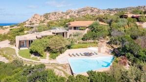 Una propiedad en una ladera con piscina, varias construcciones y vista al mar.
