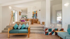 Amplia sala de estar con un sofá de madera, una mesa de comedor y una escalera que sube a un nivel superior.