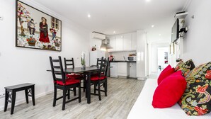 A modern kitchen with white cabinets, a dining area with a wooden table and chairs, and a living area with a sofa and decorative pillows. - Apartment Lisbon Castle area and Alfama  (Lisboa)