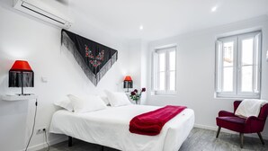 A modern bedroom with a large bed, two bedside lamps, a red chair, and a window with white curtains. - Apartment Lisbon Castle area and Alfama  (Lisboa)