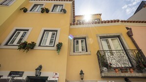 A yellow building with multiple windows, some with shutters, and a balcony with metal railings and potted plants. - Apartment Lisbon Castle area and Alfama  (Lisboa)