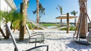 A beachside patio with white sand, palm trees, a hammock, and lounge chairs. - Resort acess - Last minute deal (Kissimmee)
