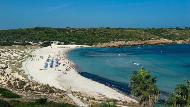 A beach with a sandy shore, clear blue water, and a path leading to a building with a white roof. - Villa Gabriel Son Parc by Villa Plus (Son Parc)