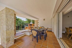 A patio area with a table set for dining, stone walls, and a view of greenery.