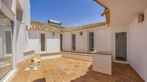 Un patio con piso de baldosas, un espacio pequeño para sentarse y una puerta.