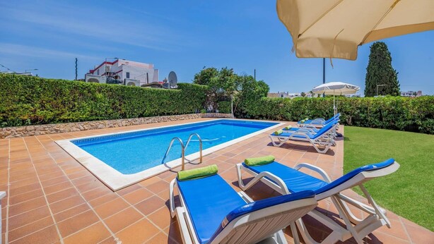 Una piscina rectangular con borde de baldosas, rodeada de sillas de descanso con cojines azules y toallas verdes.