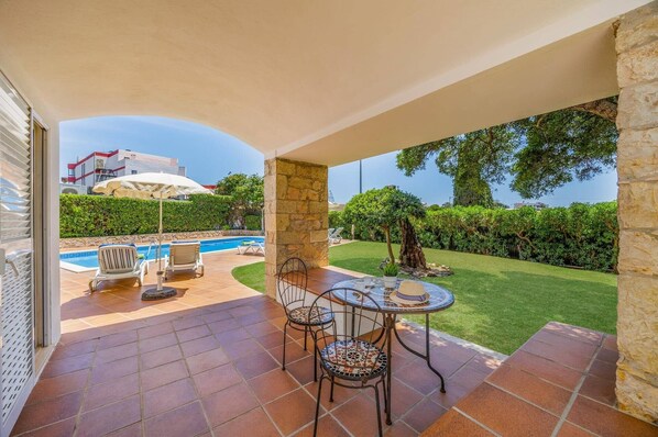 A covered outdoor area with a pool, lounge chairs, and a table with chairs. - Villa Elo by Villa Plus (Albufeira)