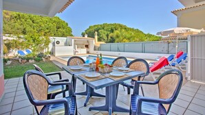 A covered outdoor dining area with a pool, chairs, and a barbecue grill. - Villa Rosa by Villa Plus (Olhos de Água)