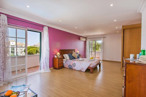 Une chambre avec une grande fenêtre, un lit en bois, une table de chevet et une armoire en bois.
