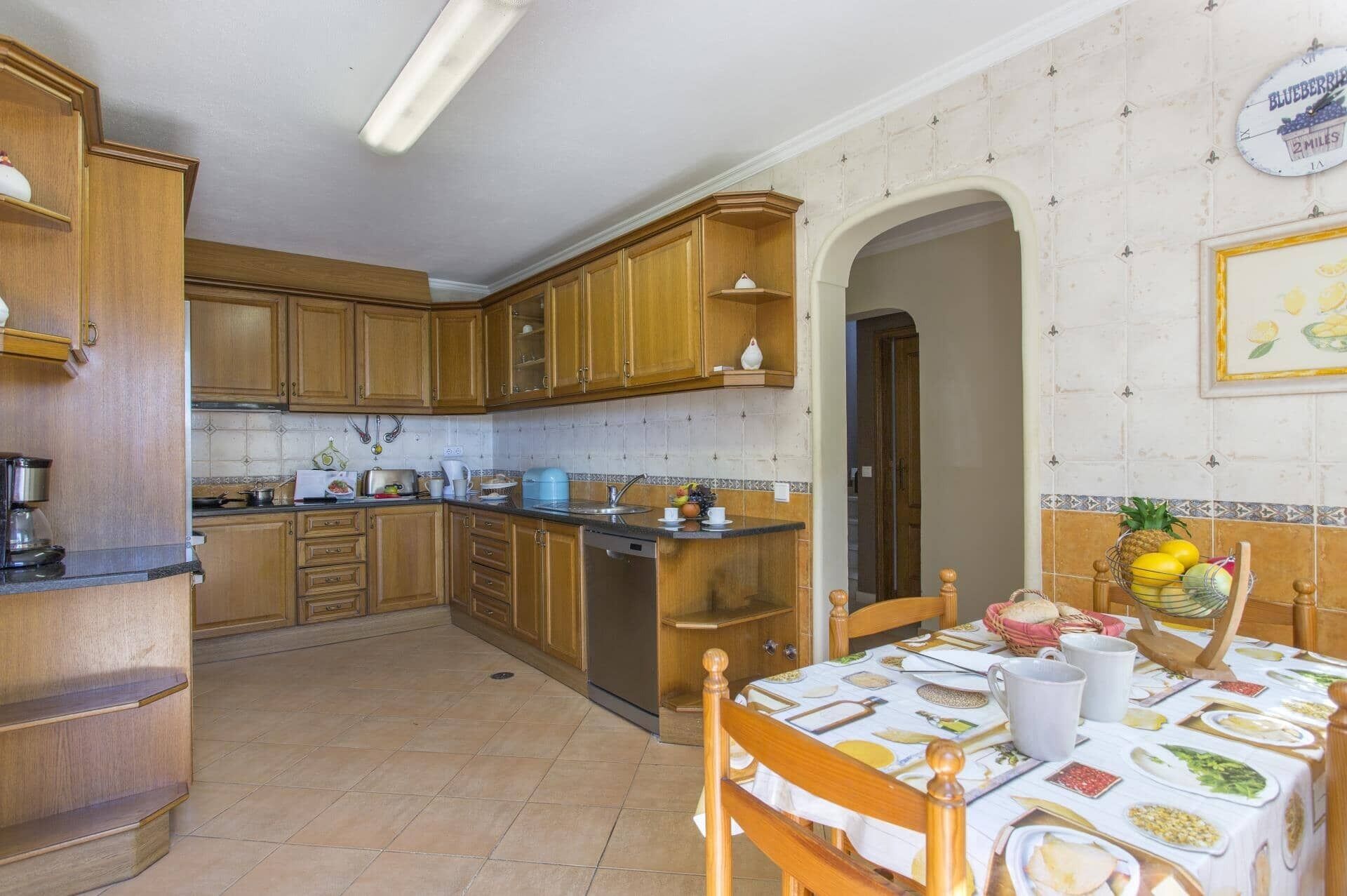 A kitchen with wooden cabinets, a dining table set with plates and utensils, and a clock on the wall.