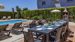 A poolside dining area with a table set for four, surrounded by lounge chairs, a barbecue grill, and a pool. - Villa Teotel by Villa Plus (Almancil)