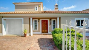 A two-story house with a tiled roof, a front door, a garage, and a small balcony with a white railing. - Villa Teotel by Villa Plus (Almancil)
