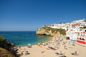 Une plage bordée de bâtiments blancs, avec une eau d’un bleu limpide et des gens qui se prélassent au soleil.