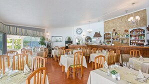 En restaurant med flere borde og stole, et barområde med hylder fyldt med flasker, og et muralmaleri på væggen.