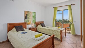 A bedroom with two wooden beds, a Buddha painting, a window with curtains, and a view of the landscape. - Villa Bali by Villa Plus (Albufeira)