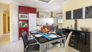 Een moderne keuken met rode kastjes, een witte koelkast en een eethoek met een glazen tafel voor vier personen.