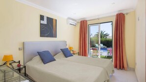 Een hotelkamer met twee bedden, een glazen tafel, een airconditioning en uitzicht op een buitenzwembad.
