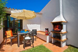 Enjoy al fresco dining on the patio with a brick oven, table, and comfortable chairs, shaded by a large umbrella.