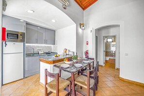 Kitchen area with central island, sink, and appliances, including a microwave and refrigerator, surrounded by dining table and chairs.