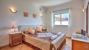 A bedroom with a bed, bedside tables, a dresser, a window with a view, and wall-mounted lights. - Villa Papi by Villa Plus (Albufeira)