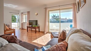 A living room with a sofa, a TV, and a table with cups. There is a balcony with a chair and a table. - Villa Papi by Villa Plus (Albufeira)
