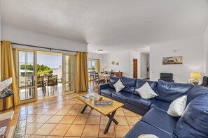 A living room with a blue sofa, a wooden coffee table, and a dining area with chairs and a table. - Villa Primavera by Villa Plus (Albufeira)