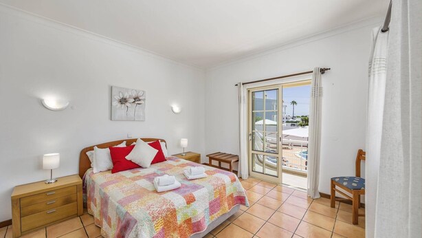 Un dormitorio con cama, mesitas de noche, una silla, una ventana con vistas y un cuadro en la pared.