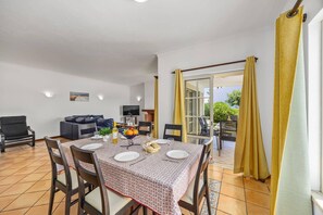 A dining area with a table set for four, a sofa, and a television in the background. - Villa Primavera by Villa Plus (Albufeira)