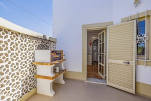 A narrow outdoor corridor with a patterned wall, a small seating area with a table and chairs, and a door leading to an interior space. - Villa Primavera by Villa Plus (Albufeira)