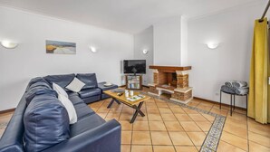 Una sala de estar con sofá, televisión, chimenea y piso de baldosas.