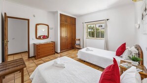 Habitación de hotel con dos camas, un armario de madera, un espejo, una ventana con cortinas y un banco.