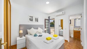 Una camera da letto con un letto, comodini, un tavolino da notte, una finestra con tende e bagno con specchio, oltre a un condizionatore d'aria.