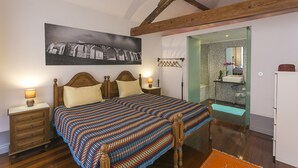 A bedroom with a large bed, wooden headboard, bedside tables with lamps, a framed picture on the wall, and a view into the bathroom.
