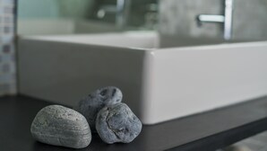 A bathroom with a white sink and a mirror. There are three gray stones on the countertop.