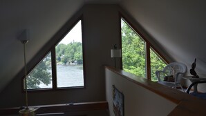 A room with a view of a lake, a white chair, a table, and a lamp.