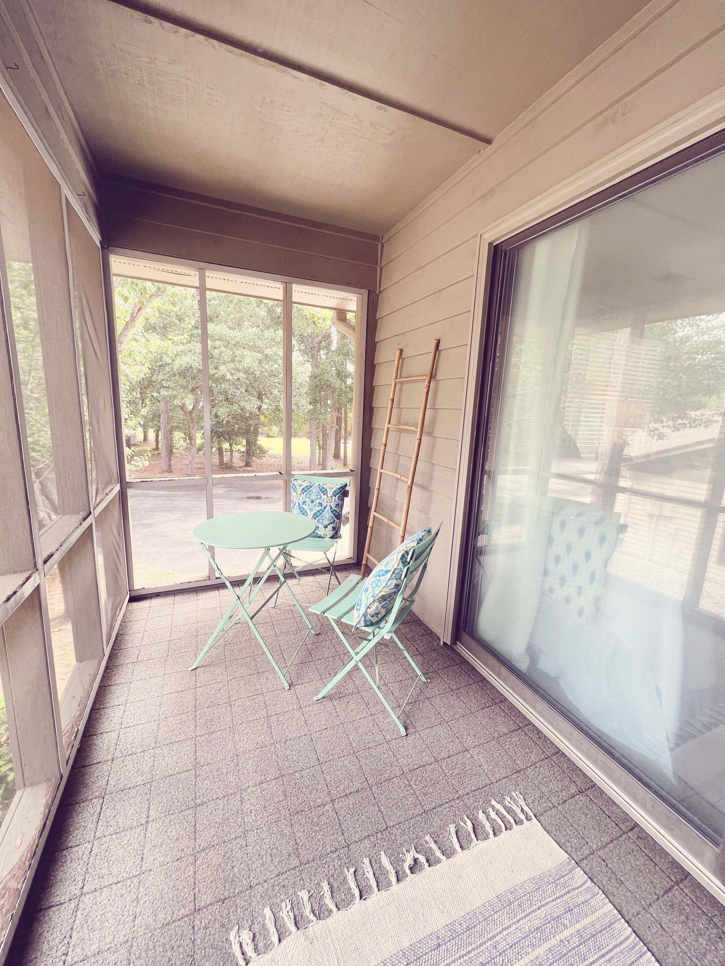 A sunlit room with a sliding glass door, a small table with chairs, and a patterned rug on the floor.