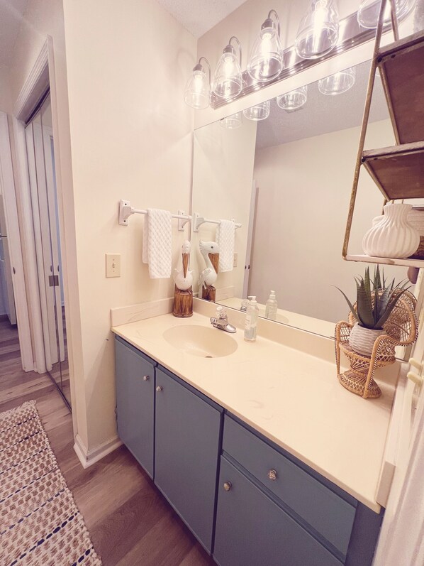 A bathroom with a white sink, a mirror, and a shelf with decorative items.