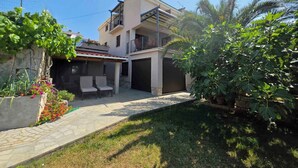 A two-story residential building with a covered patio area, outdoor seating, and lush greenery.