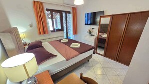 A hotel room with a bed, a desk, a chair, a TV, and a wardrobe.