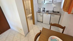 A compact kitchen with white cabinets, a sink, and a coffee maker. A wooden door leads to a shower area.