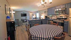 A compact kitchen with a dining table, chairs, a refrigerator, microwave, oven, and a chandelier.