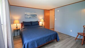 A bedroom with a bed, two bedside lamps, a wooden chair, a wooden wardrobe, and a painting on the wall.