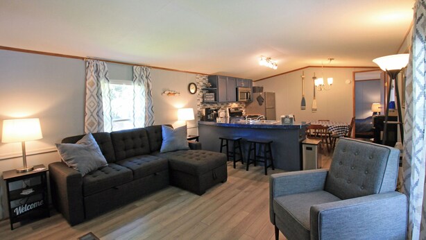 A modern living room with a sectional sofa, a grey armchair, and a small kitchen area with a microwave and refrigerator.