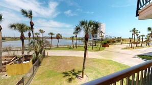 A view of a waterfront area with palm trees, a building, and a body of water. - Maravilla Seawall Condo by AB Sea (Galveston)