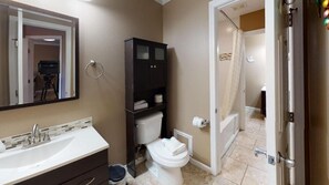 Un baño con lavamanos blanco, muebles oscuros, un inodoro y una zona de ducha.