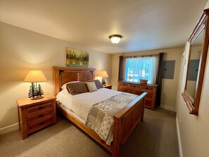 A bedroom with a wooden bed, two bedside tables with lamps, a window with curtains, and a painting on the wall. - Great downtown Sandpoint location! (Sandpoint)