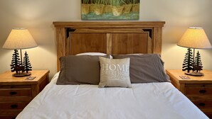 Ein ordentlich bezogenes Bett mit einem Kissen, auf dem "HOME SWEET HOME" steht, und zwei Nachttische mit Lampen und lampenschirmförmigen Bäumen.