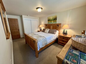 A bedroom with a wooden bed, two bedside tables with lamps, a small table with a mirror, a wall-mounted painting, and a door.