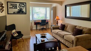 Ein Wohnzimmer mit einer Couch, einem Couchtisch, einem Schreibtisch mit Stuhl, einer Lampe und einem Poster an der Wand.