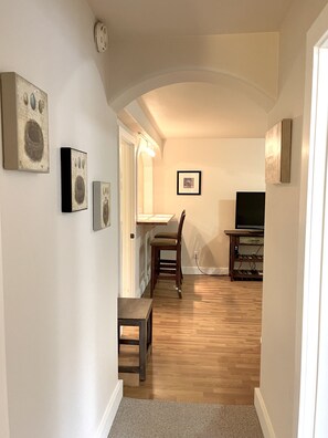 A hallway with a wooden floor, a dining area with a table and chairs, and a TV stand.